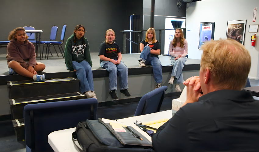 Students performing Frozen Jr. on stage with Arendelle castle backdrop and sparkling snow effects